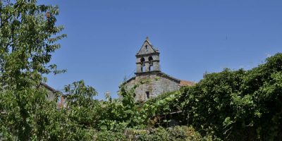 La espadaña de la iglesia de San Munio da Veiga (A Bola, Ourense) se yergue sobre la vegetación que rodea el pueblo