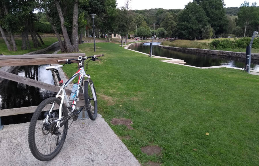 Bici de montaña en el área recreativa y fluvial del río Orille, con césped rodeado de árboles y adaptado como piscina